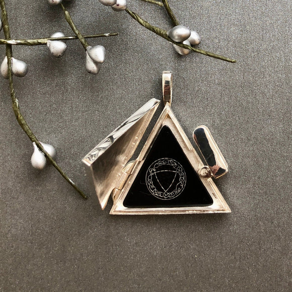 Triangular pendant with black center and emblem on a gray surface with willow branches.