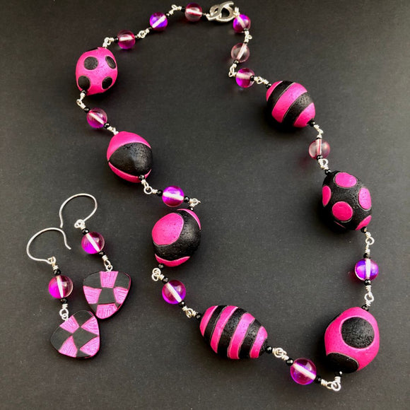 Necklace and earrings set with pink and black beads on a dark background